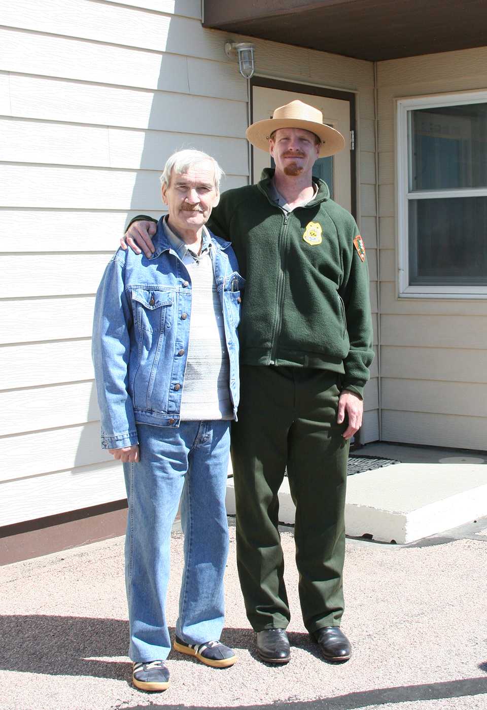 Stanislov Petrov at Delta-01 Elderly man and a park ranger stand outside a tan building.