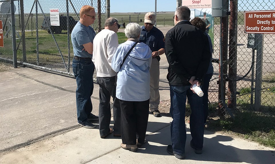 A volunteers speaks to a small tour group at a fenced gate