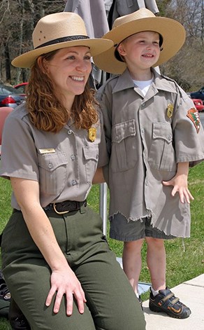 Kneeling ranger poses for a photo with a child in oversized ranger uniform