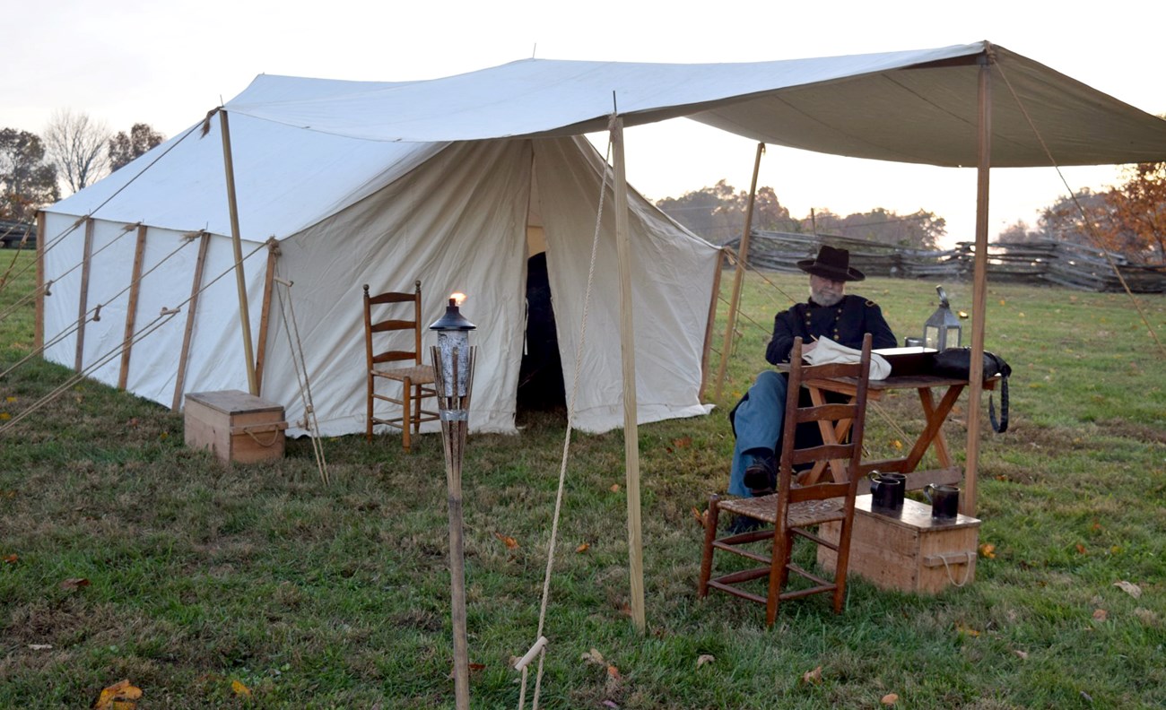 Civil War reenactor studies documents at a field desk under canvas tent