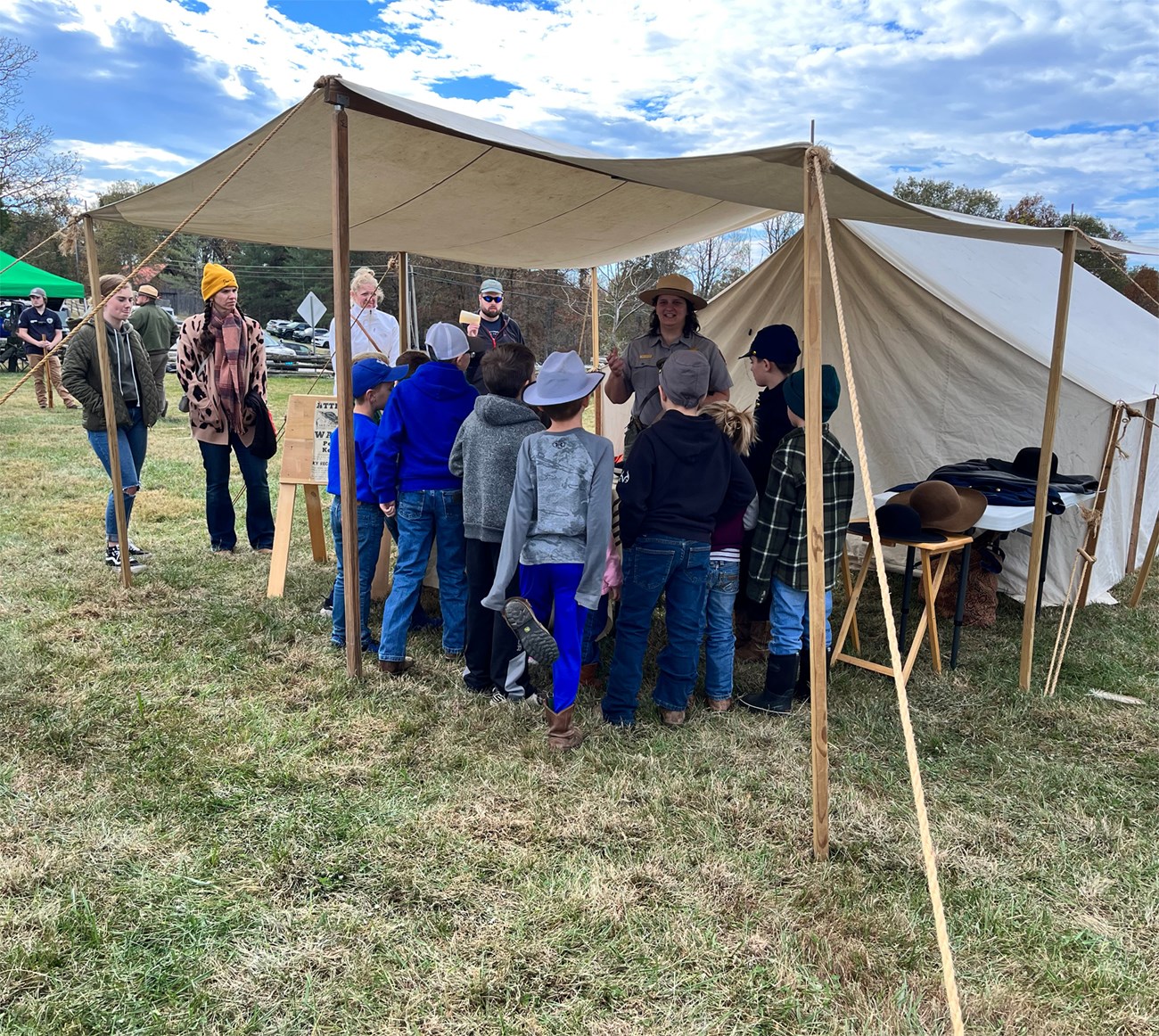 A group of kids standing in front of a table under a tent talking with a park ranger.