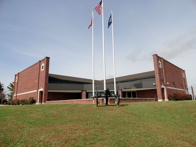 A low-level, red brick building in green grass with flag poles in front
