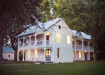 Two-story antebellum home at dusk with lighted, glowing windows