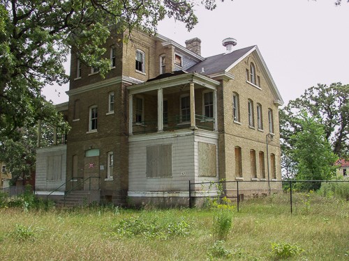 On old building stands in a weedy yard.