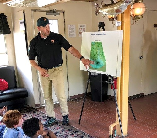 A river educator points to an easel. An NPS educator directs the attention of students to a graphic on an easel.