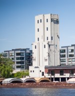 A tall white shoreline commercial building with barge traffic passing it front of it.