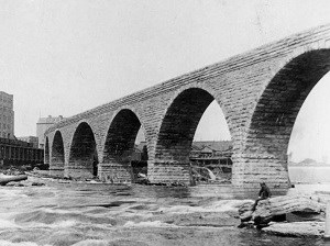 A bridge made from stone and being carried by great arches crosses the river.