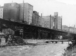 Mill buildings line the river above an elevated rail line.