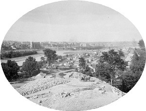 Saint Paul lies across the river from the mine pits in the foreground. The Mississippi River flows between the stone quarries  and the city.