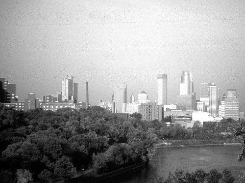 The Minneapolis skyline towers over the wooded gorge and the river.