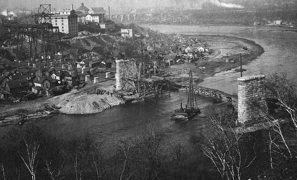 A large river cuts between bluffs on which sits a city. A flat area sits at the bottom of bluff on which there are houses.