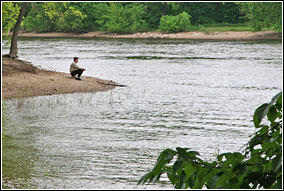 A man sits at the edge of an island in quiet contemplation. The Mississippi and Minnesota Rivers converge here in among tree-lined shores. A man sits at the edge of an island in quiet contemplation. The Mississippi and Minnesota Rivers converge here in among tree-lined shores.