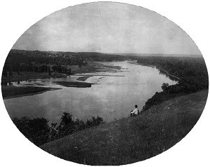 A man sits on a river bluff contemplating the river below.