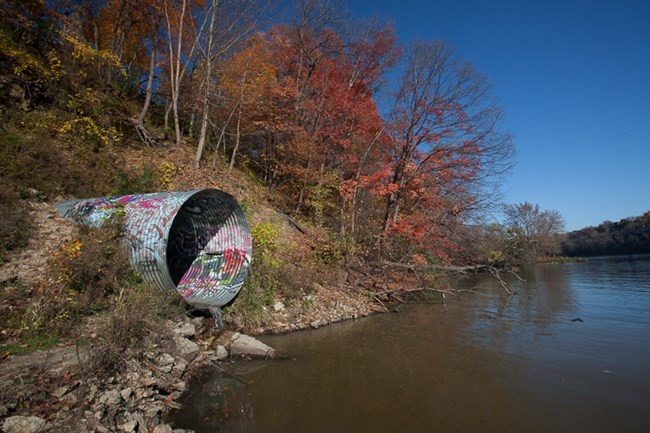 A large culvert or pipe hangs out over the river. A large culvert or pipe hangs out over the river.