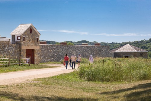 A group of people walk past a stone-walled fort.