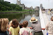 A uniformed NPS Ranger pointing up the river at the city skyline. Children looking in the same direction.