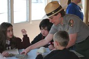 A uniformed ranger helps students with a geology lesson.