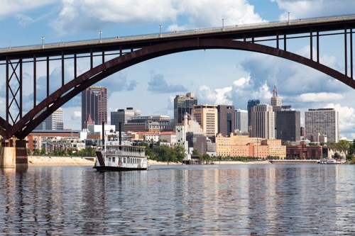 A paddlewheeler passes beneath a bridge on a wide river.