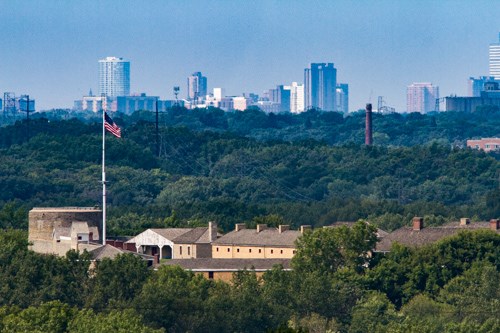 A view among forested hills and an old fort and a modern downtown area.