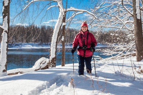 A person in a red coat hiking in a snow-covered forest. A large river is in the background.