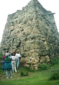 Several people stand in front of a square stone tower.