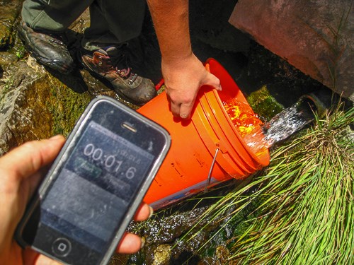 A bucket is held under a water stream and a stopwatch is used to determine time.