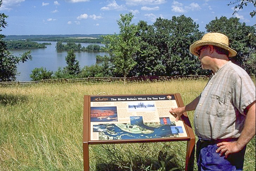 A man looks at an exhibit overlooking a lake. A man looks at an exhibit overlooking a lake.