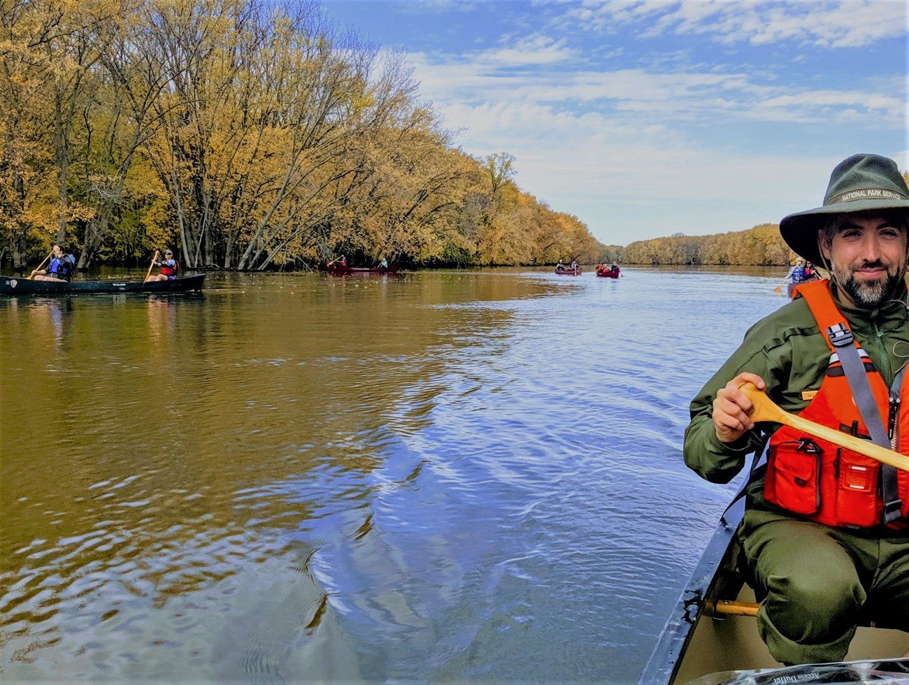 People in kayaks on a river during a fall day.