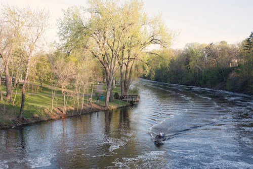 A motorboat passes a quiet park on a river.