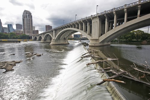 A bridge crosses a waterfall with a city skyline in the distance.