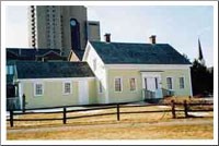 Small light colored house with a smaller house attached. Tall apartment building in background