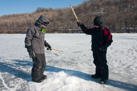 Two boys ice fishing on a snow-covered lake flanked by forested hillsides. Two boys ice fishing on a snow-covered lake flanked by forested hillsides.