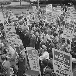 Black and white photograph of people marching holding holding signs