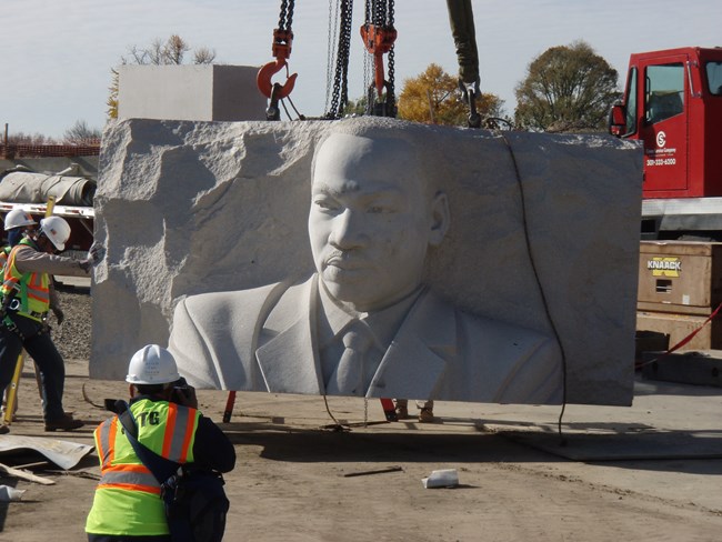 A granite slab with MLK's likeness is lifted by crane