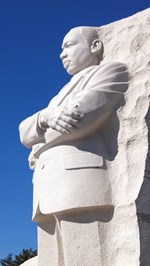 Statue of man folding his arms looking off in the distance coming out of a large stone