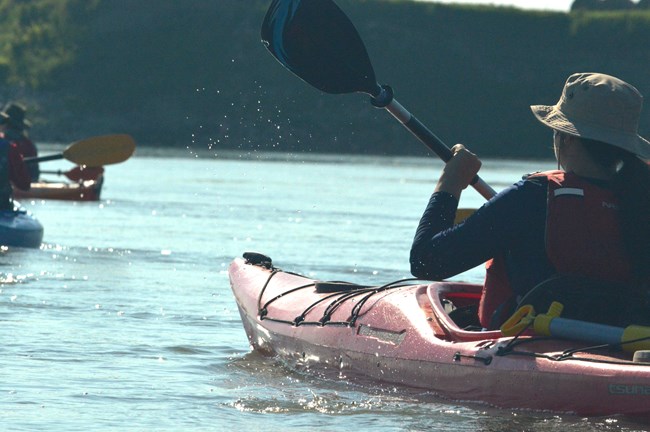 A kayaker paddlles towards other kayakers on the water.