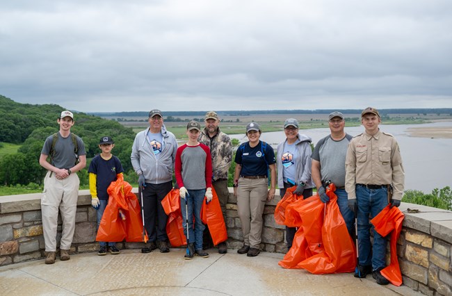 Nine people stand together at a scenic overlook, some hold trash bags and grabbers.