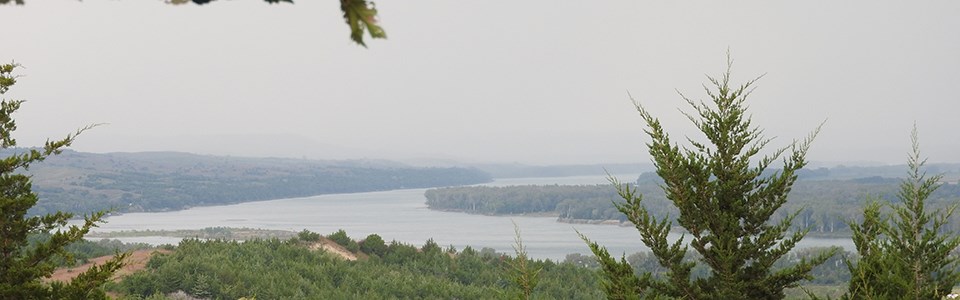 View above a river valley of eastern red cedars and the Missouri River in the background.