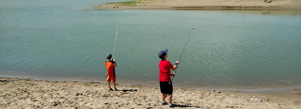 Two kids with their fishing poles are trying their luck with fishing the river.