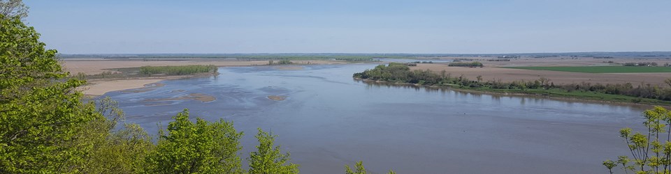 A wide view of the Missouri River with its borders outlined by cottonwood trees.