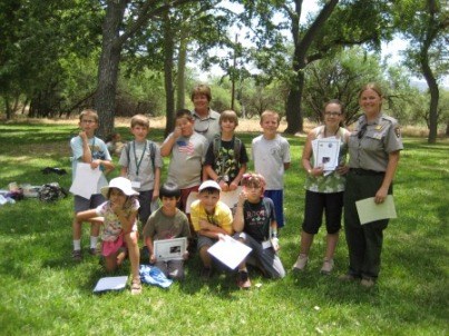 Ten children with certificates pose with two adults in a grassy park. Ten children with certificates pose with two adults in a grassy park.