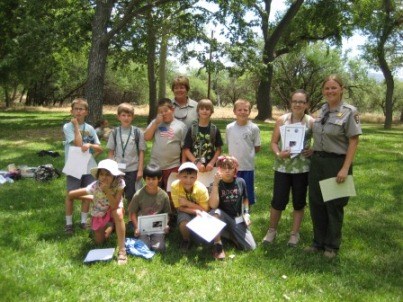 Ten kids with certificates pose with two adults in a grassy park.