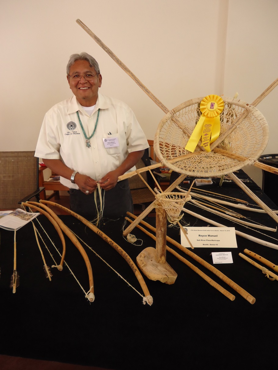 Royce Manuel sits behind a table with traditional arts and technologies.