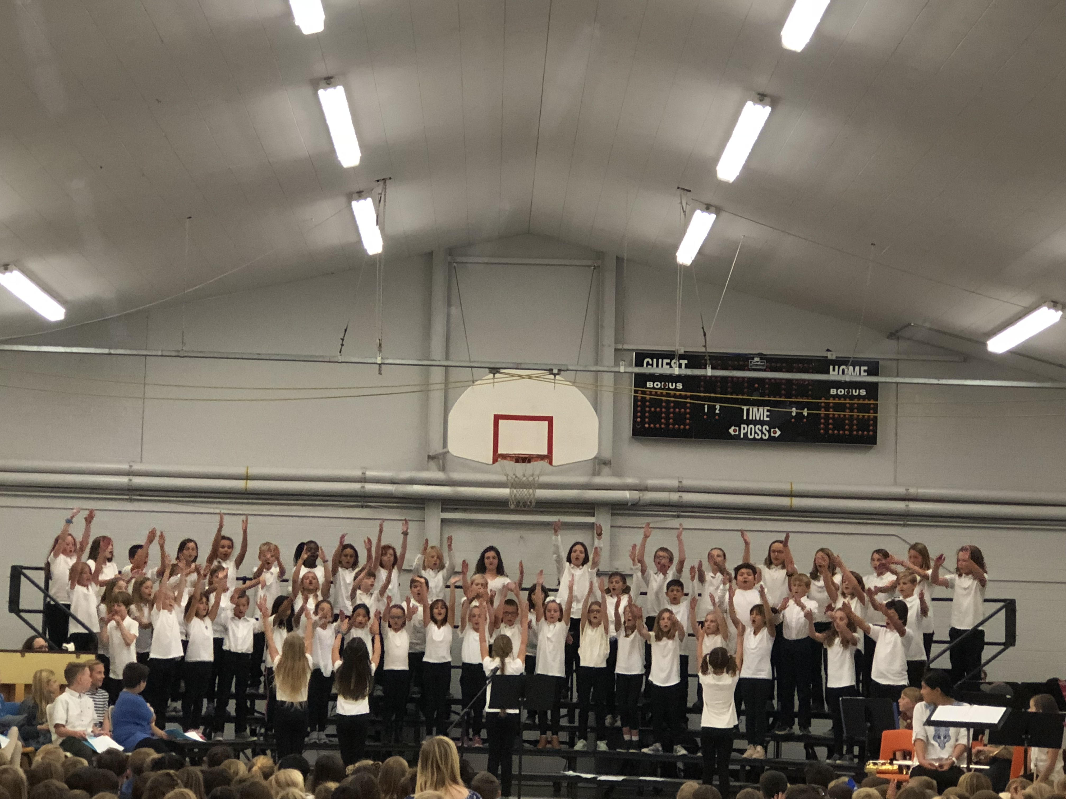 Children standing on risers, all in black pants and white shirts, singing.