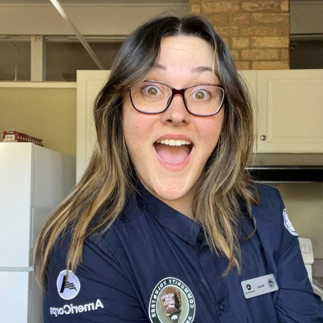 Woman in a blue polo shirt sitting inside smiling.