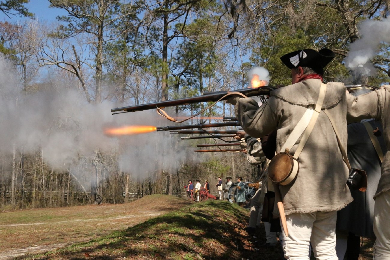 Several soldiers firing muskets behind earthworks