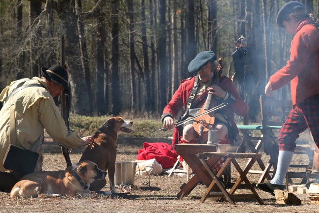 Man play a bowed dulcimer around campfire