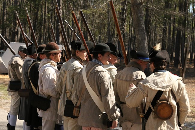 Men in formation facing away with trees in background