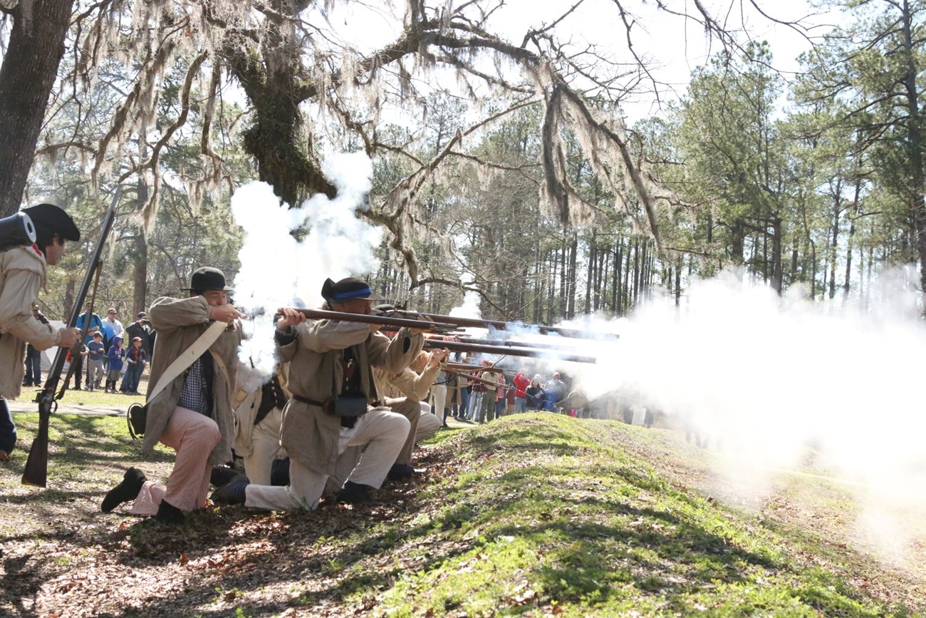 Men firing muskets behind earthworks