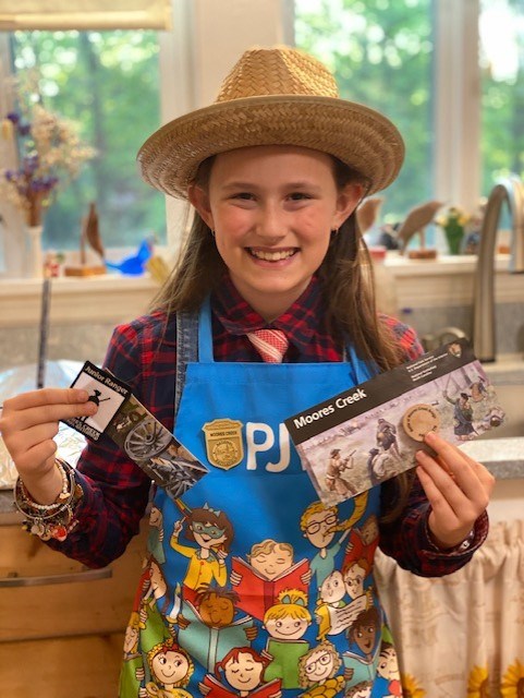 A Female Junior Ranger holding up a patch, wooden nickel, and bookmark.